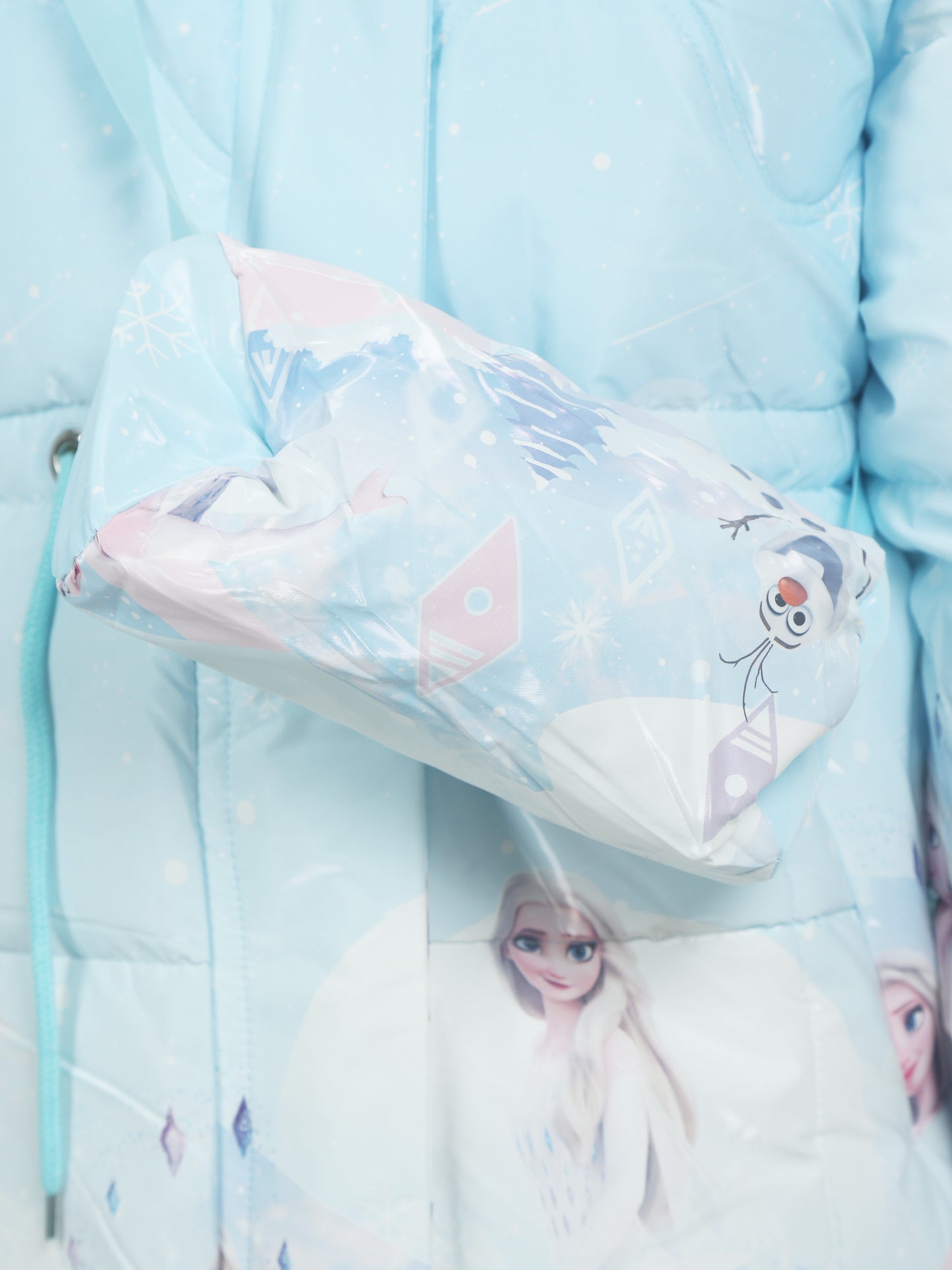 Close-up of a light blue Frozen-themed crossbody bag featuring Olaf and Elsa prints, worn over a matching winter jacket with snowflake and diamond patterns.