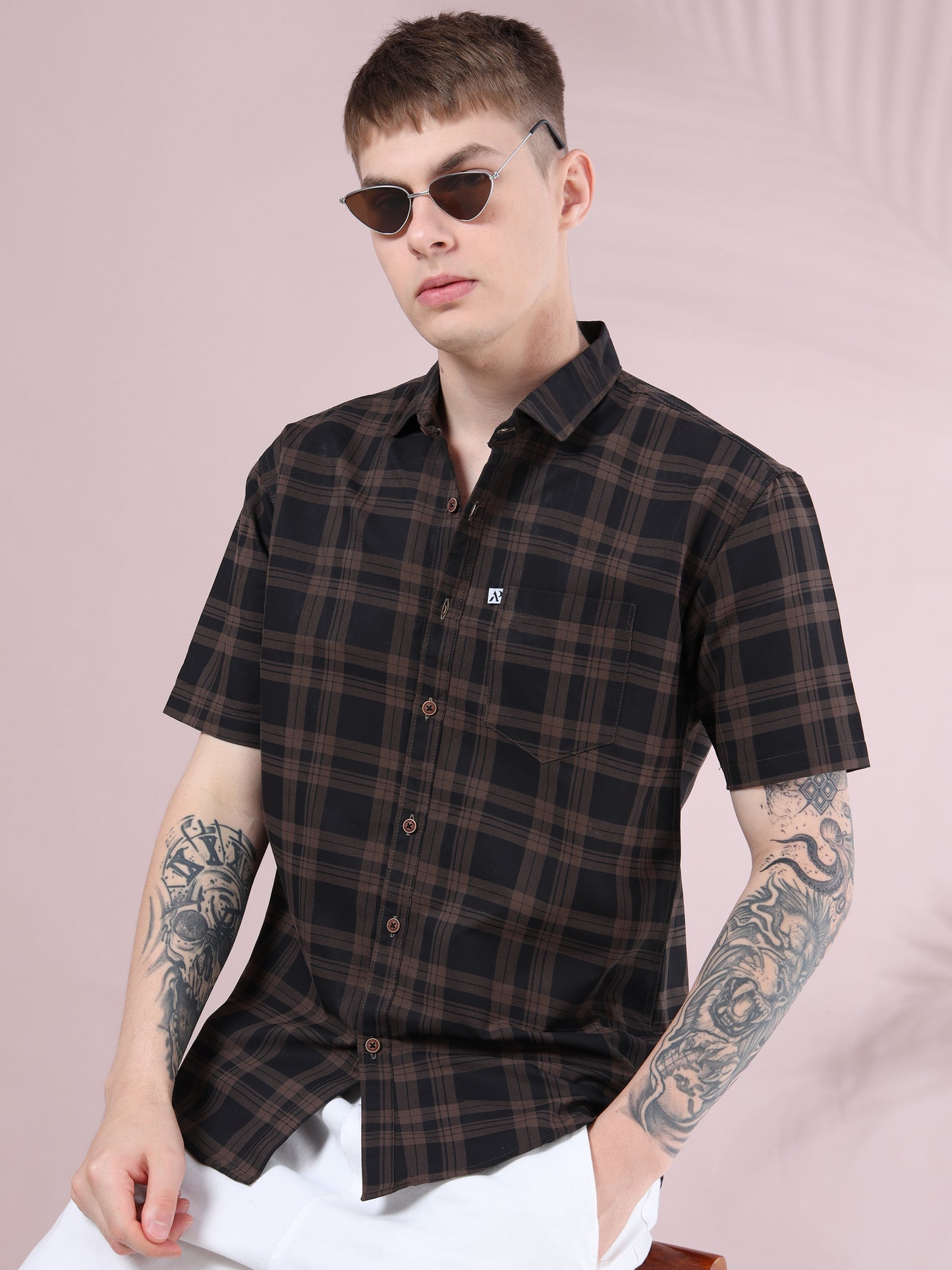 Men’s brown and black checked short sleeve cotton shirt styled with white pants and sunglasses.