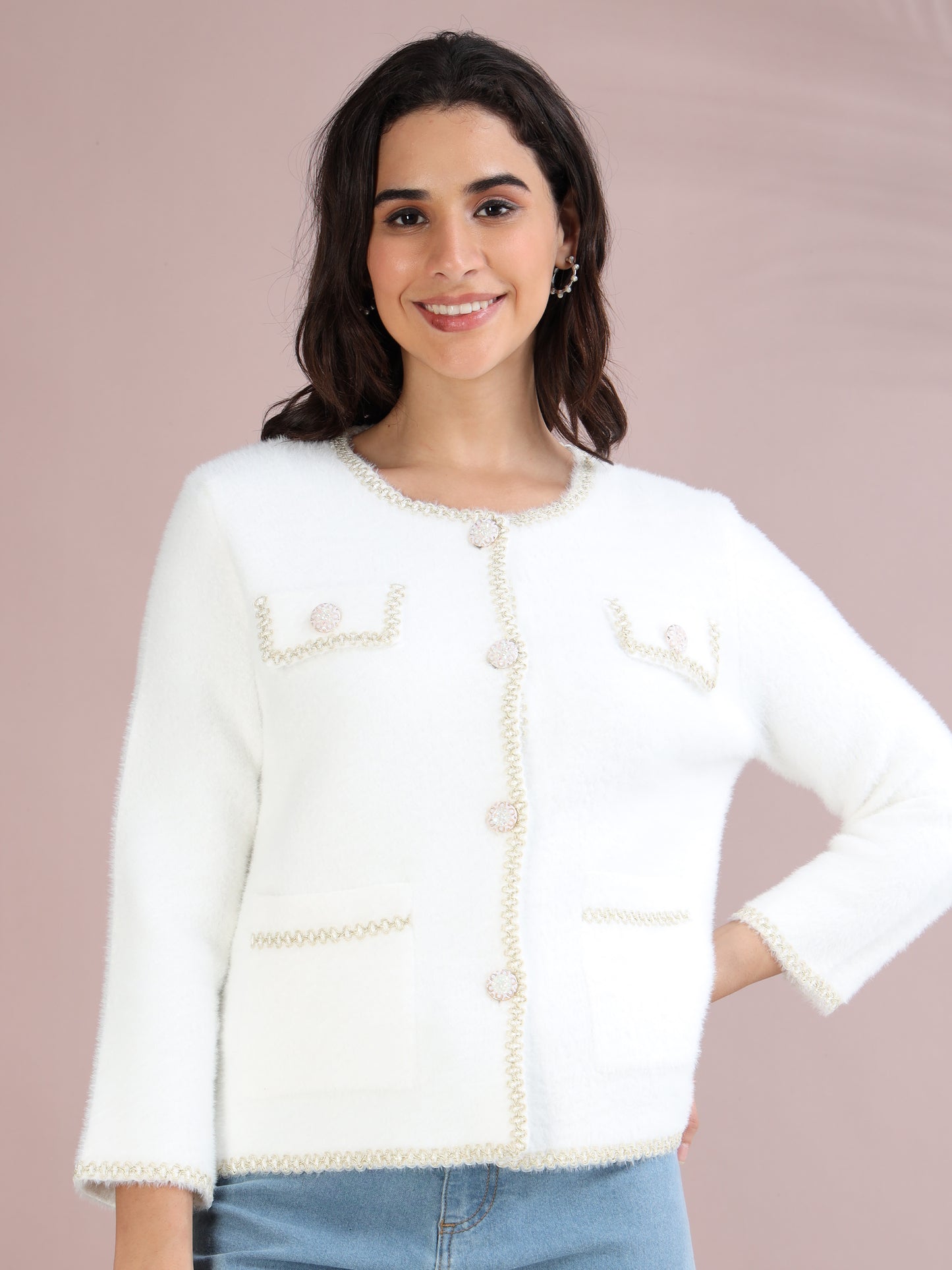 Woman wearing a white knitted cardigan with pearl buttons and front pockets, styled with blue jeans.