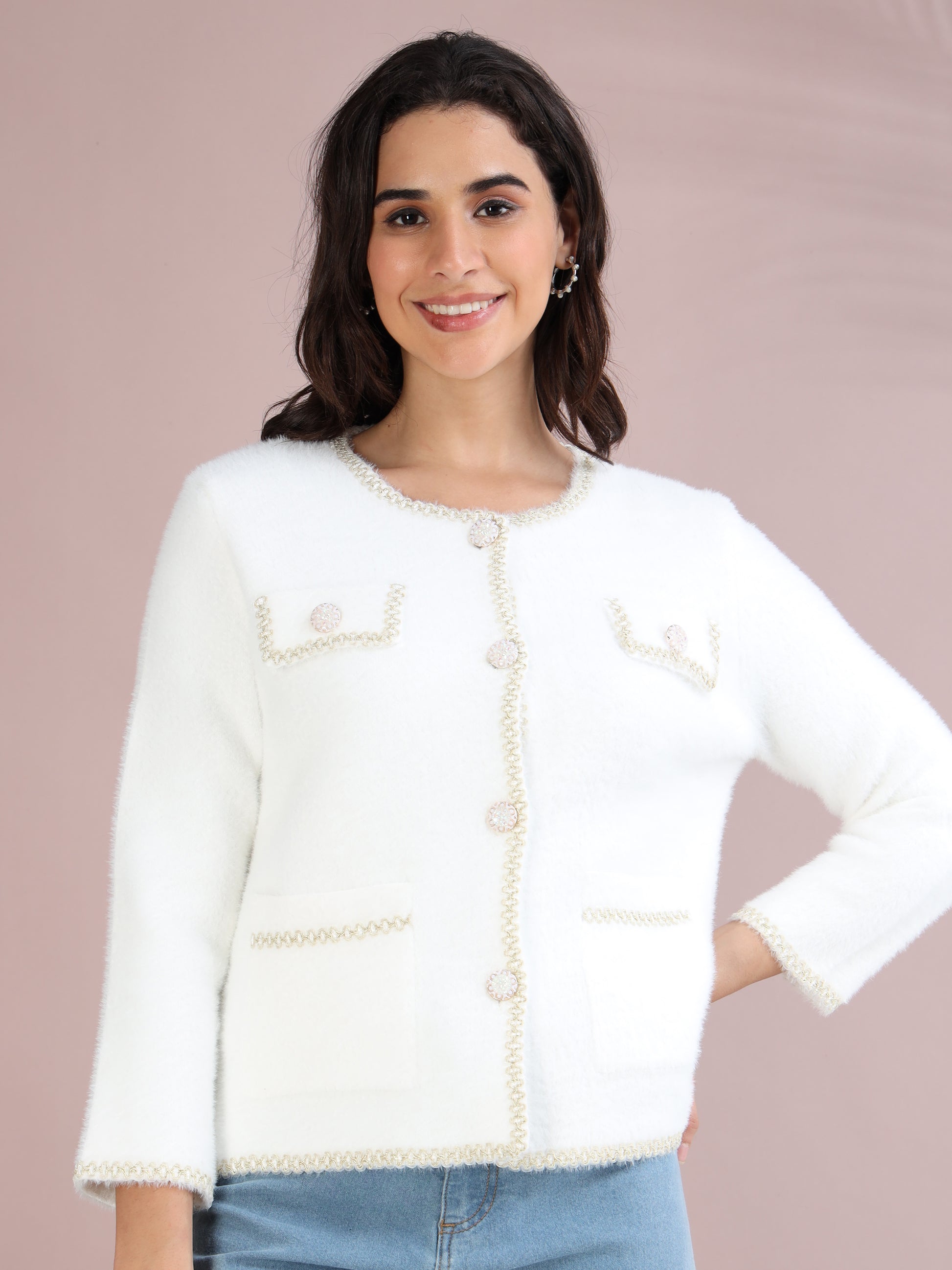 Woman wearing a white knitted cardigan with pearl buttons and front pockets, styled with blue jeans.