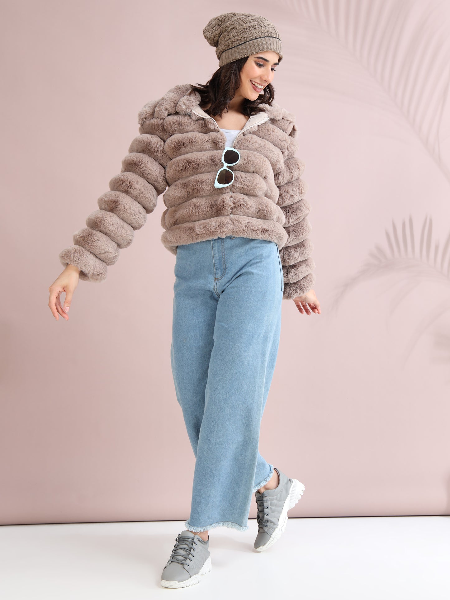 Woman in beige faux fur jacket styled with beanie, sunglasses, and wide-leg denim jeans for winter fashion