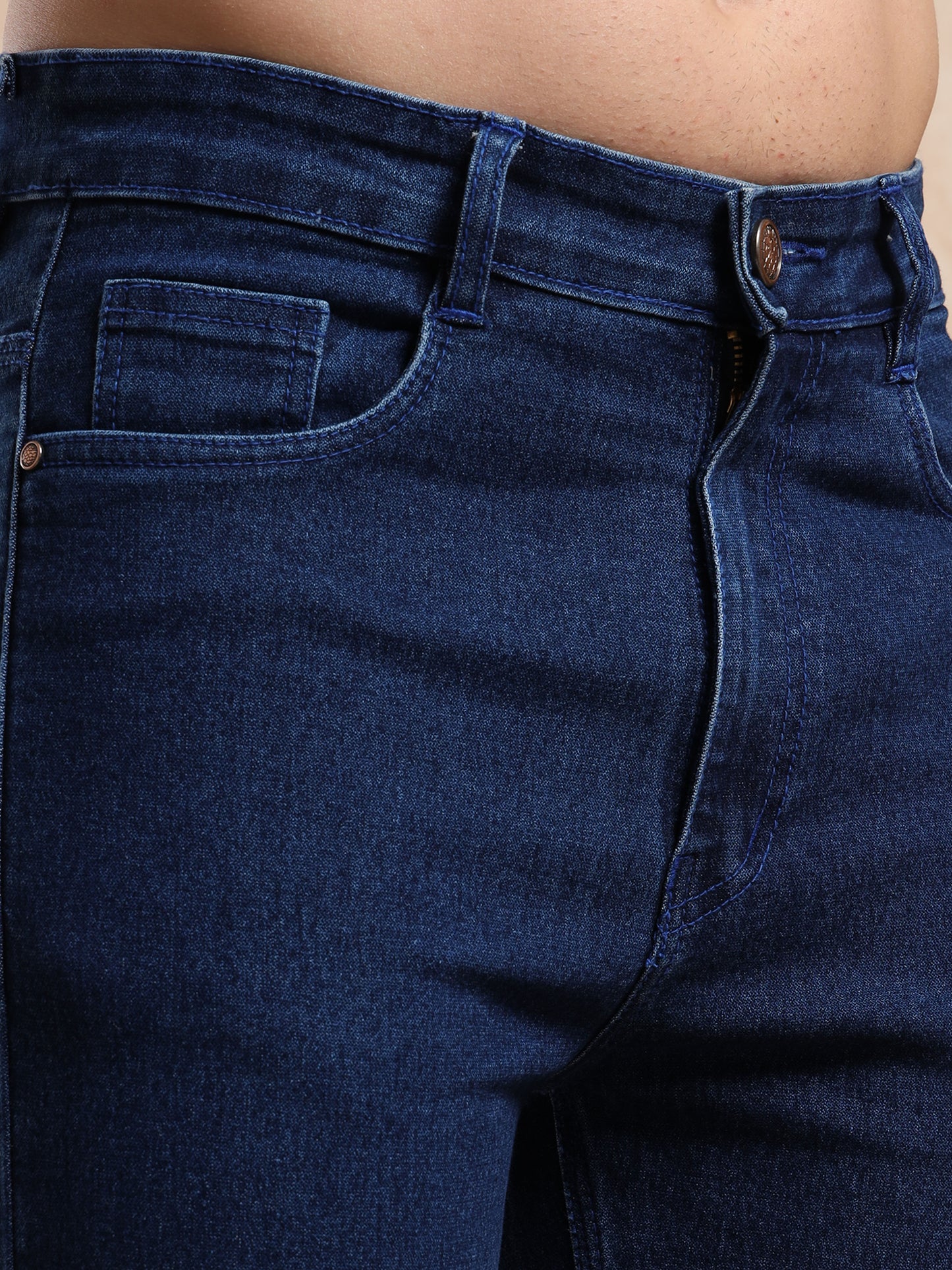 Detailed close-up of coin pocket and button closure on slim fit dark blue jeans