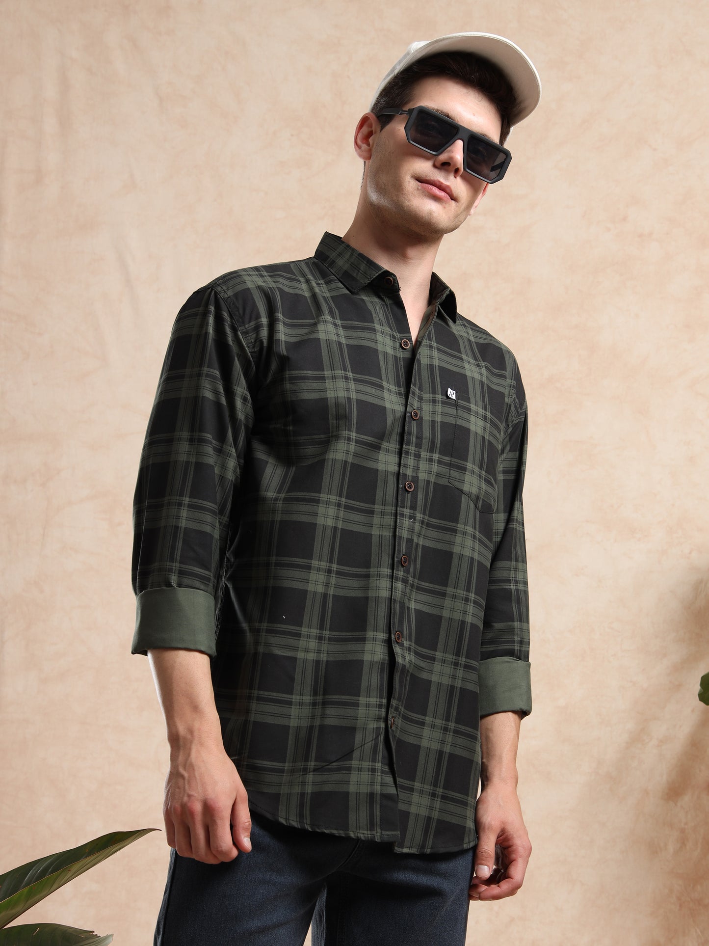 Casual men’s green check shirt styled with white cap and sunglasses.