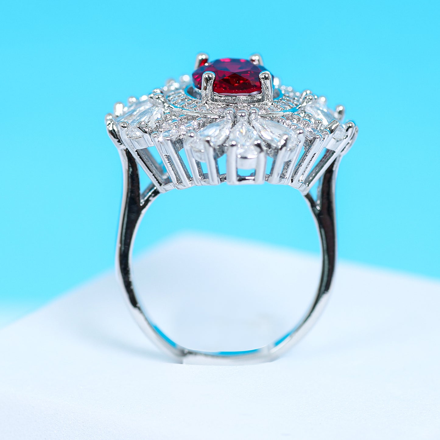 Side profile of an exquisite ruby red zirconic stone ring with a halo of pear-cut and round white crystals