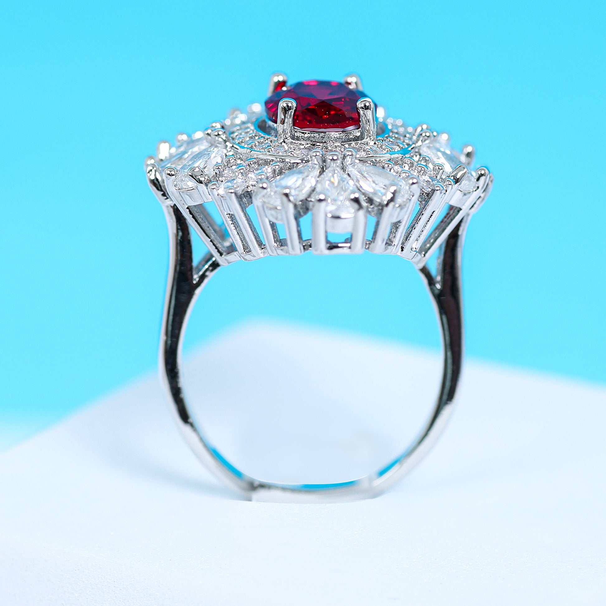 Side profile of an exquisite ruby red zirconic stone ring with a halo of pear-cut and round white crystals