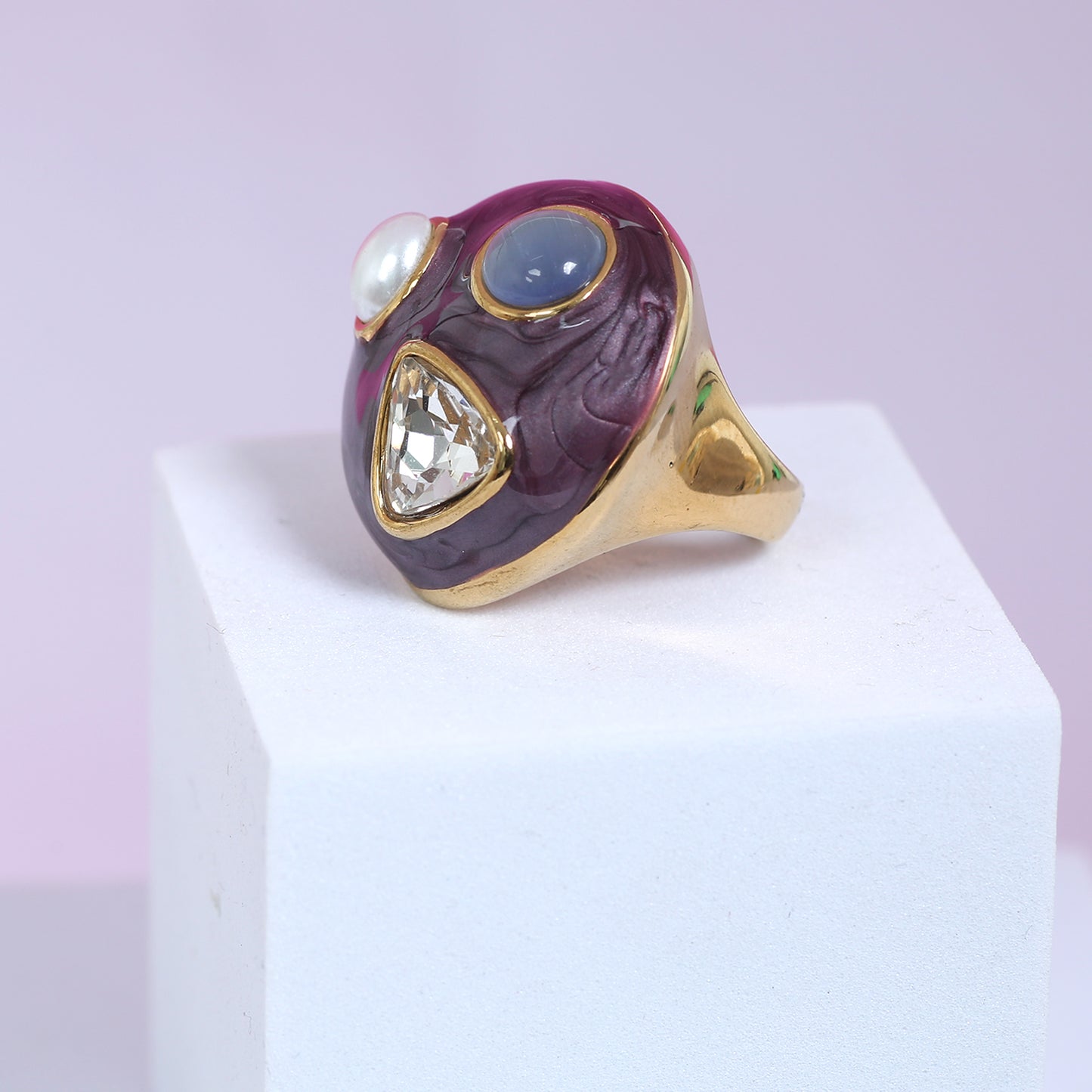 Close-up of luxury gold-plated maroon enamel ring featuring pearl, blue gemstone, and diamond-cut crystal