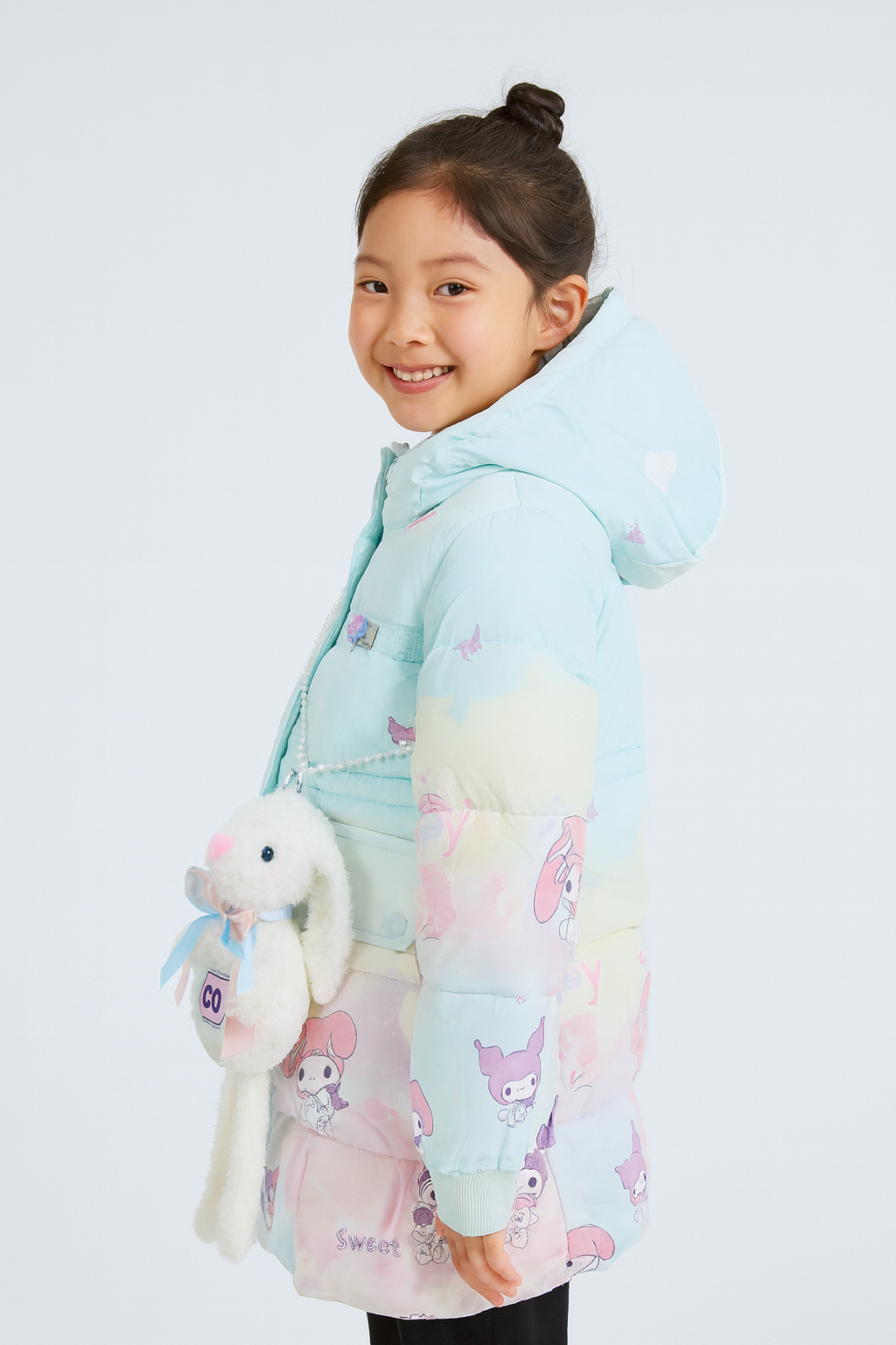 a pastel-colored puffer jacket with a hood, featuring mint green, pink, and yellow tones and decorated with My Melody and Kuromi cartoon prints. ,holding a plush white bunny bag with a blue ribbon