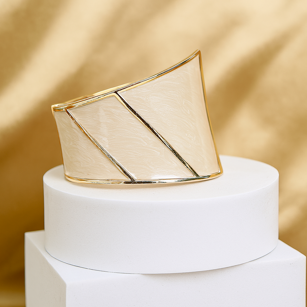 Stylish asymmetric gold cuff bracelet with smooth ivory enamel panels, placed on a white pedestal against a golden backdrop