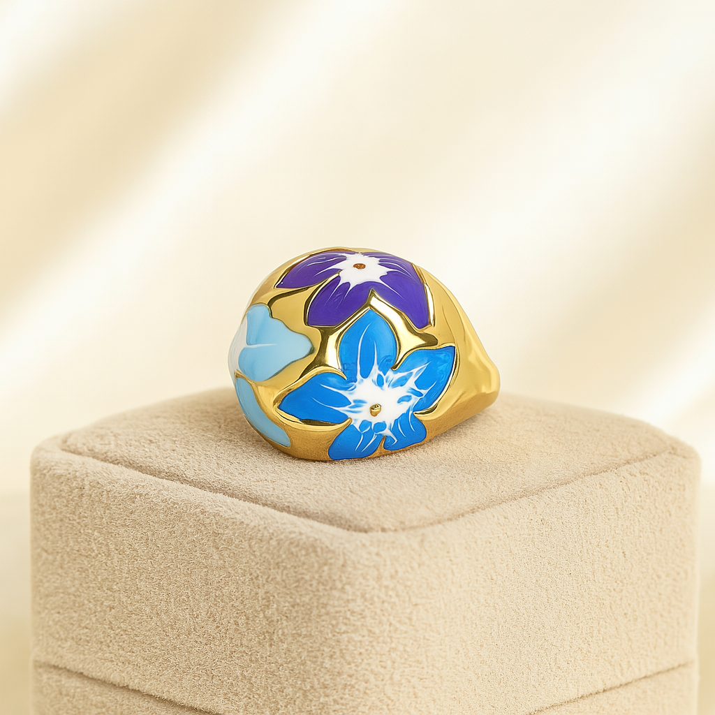Gold floral enamel anti-tarnish ring with blue and purple petals on beige velvet jewelry stand