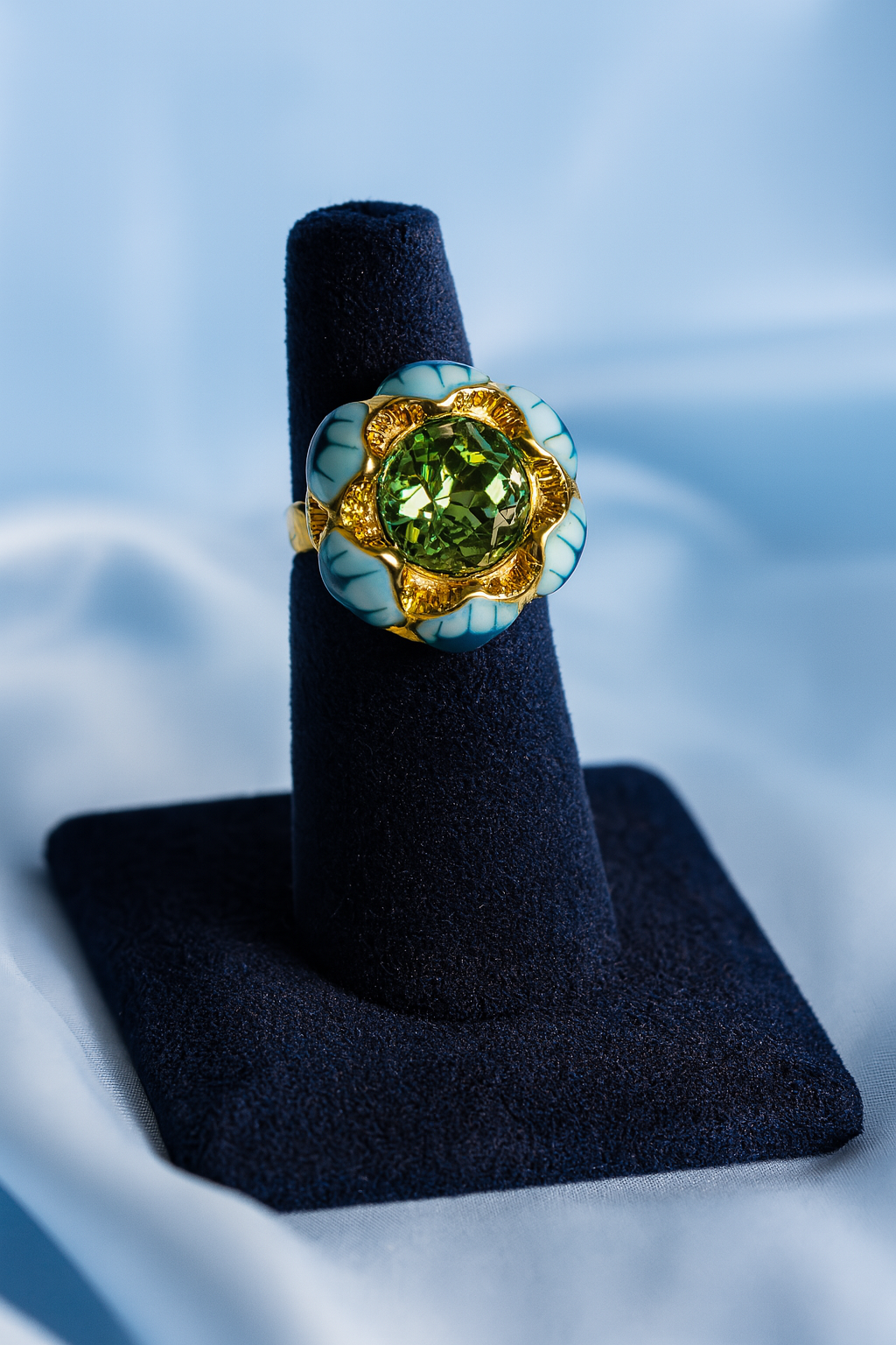 Luxury gold-plated ring with a green crystal centerpiece and turquoise enamel petal details