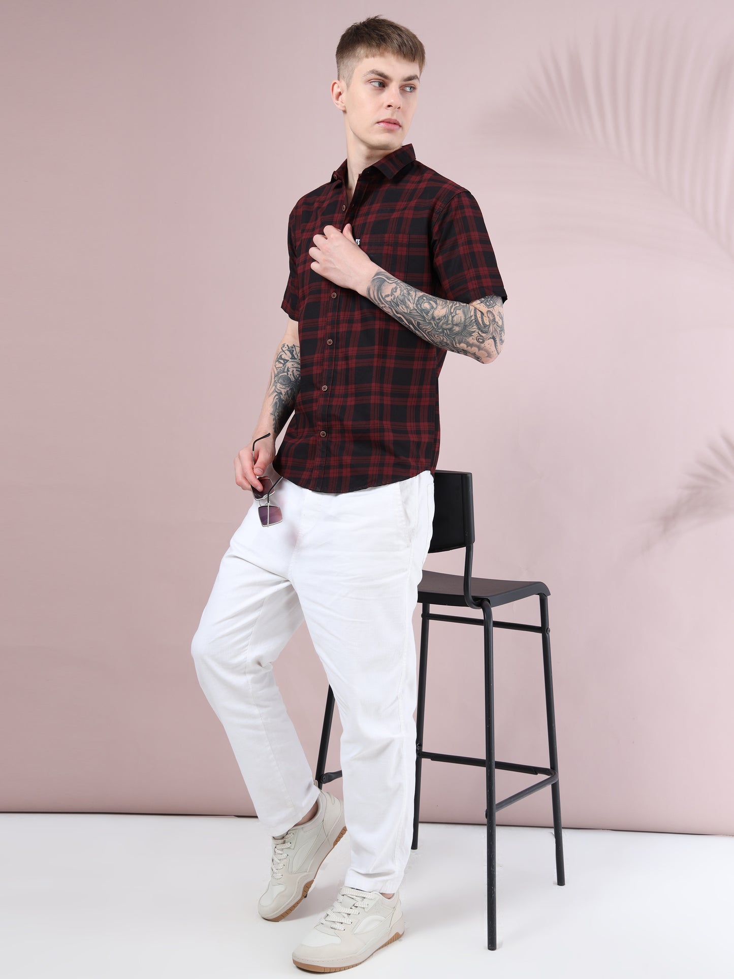 Full body view of men, maroon and black checked short sleeve shirt styled with white pants and sneakers.