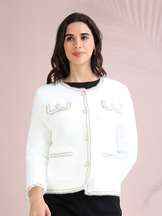 Woman wearing a white pearl button cardigan with decorative trim and front pockets, styled with black pants.
