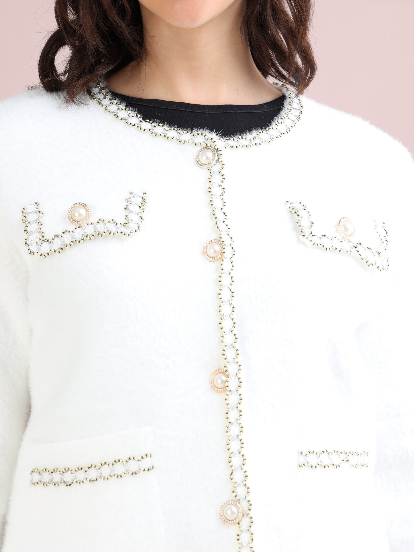 Close-up of pearl button detailing and decorative trim on white cardigan with pockets.