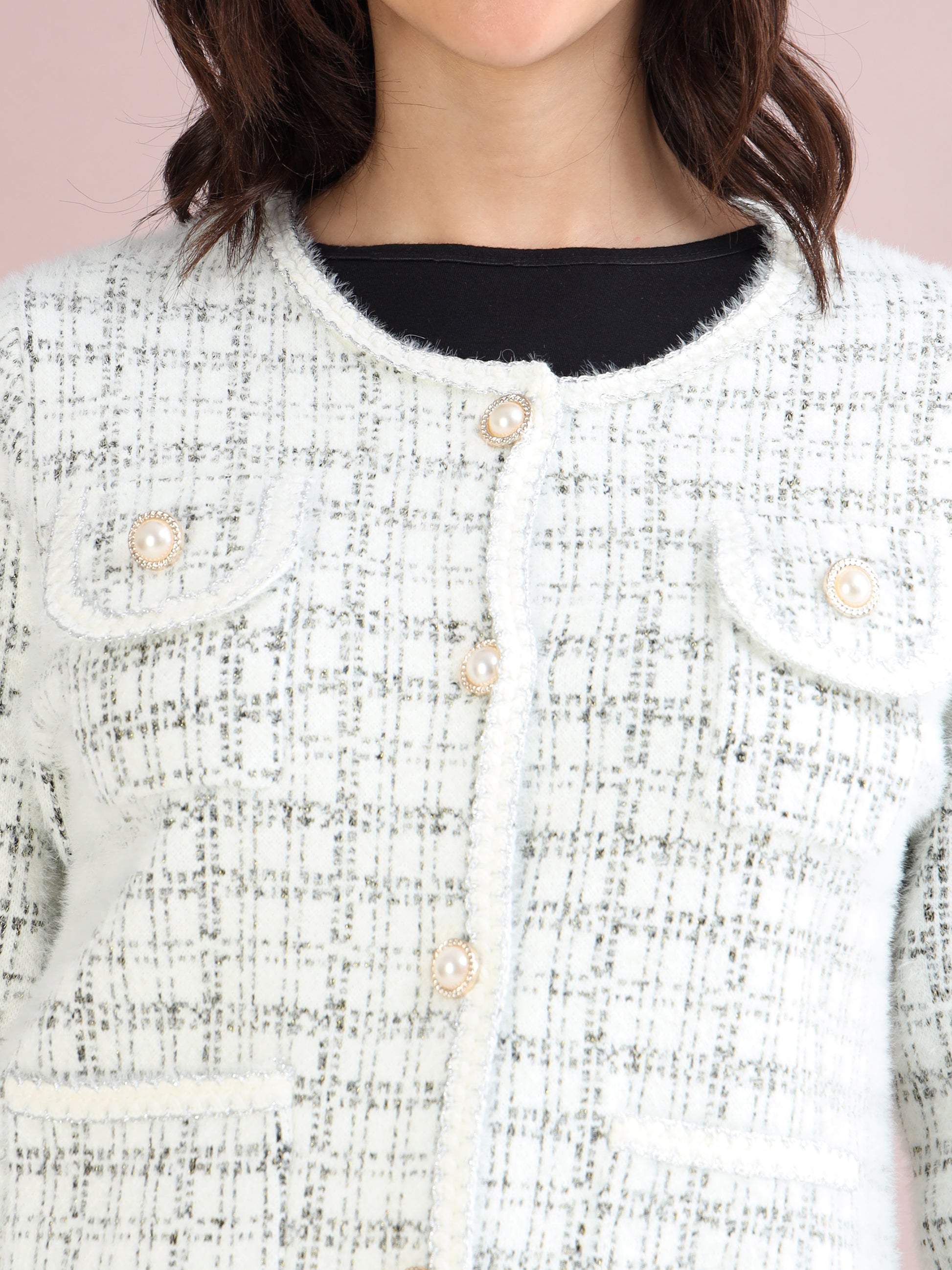 Detailed close-up of pearl button and textured tweed fabric on white women’s cardigan.