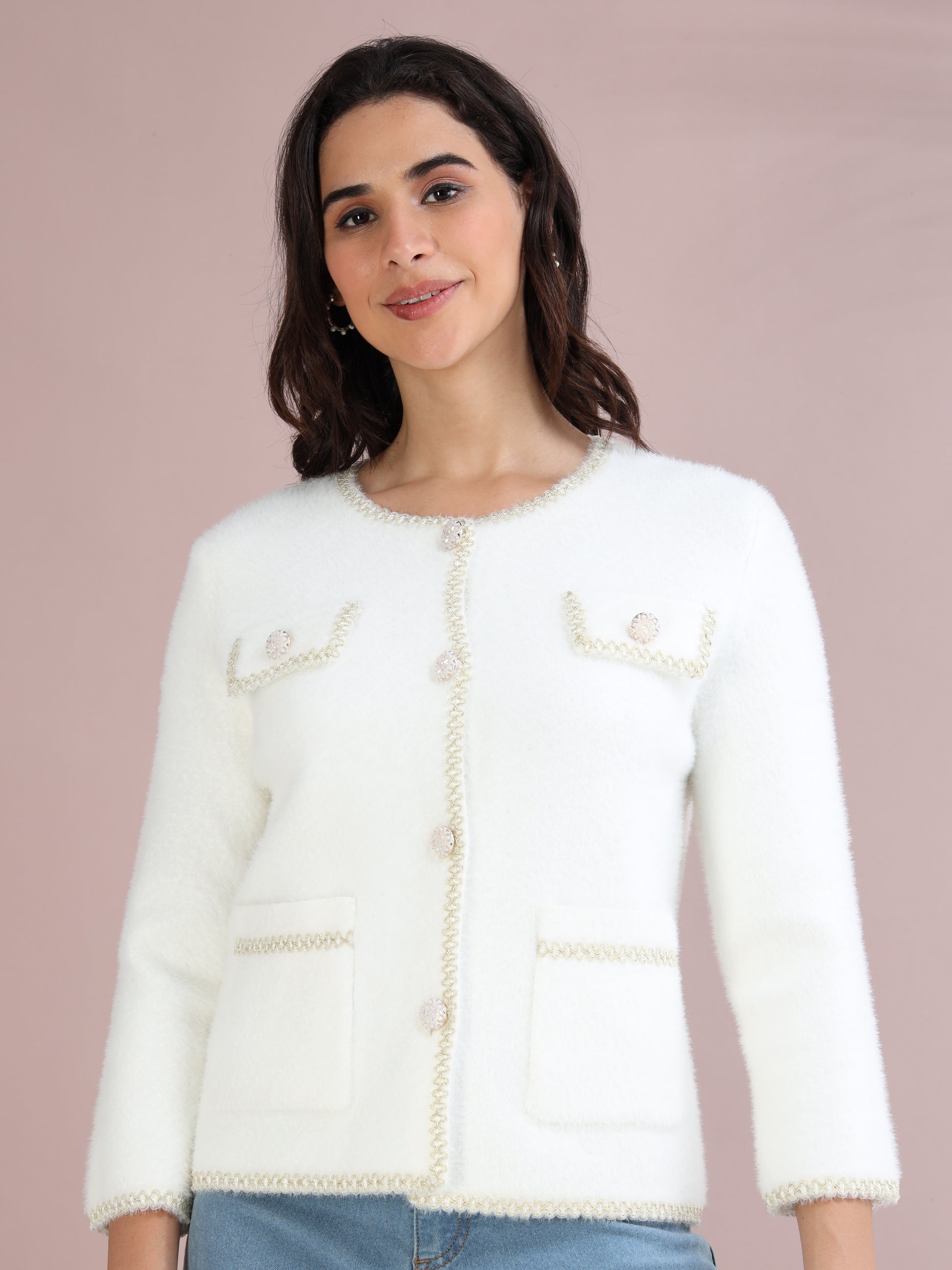 Woman wearing a white knitted cardigan with pearl-style buttons and pocket detailing, styled with blue jeans