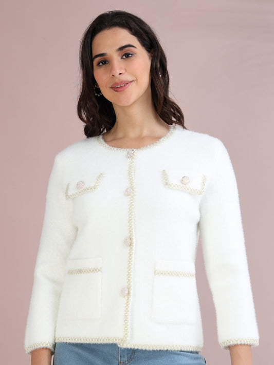 Woman wearing a white knitted cardigan with pearl-style buttons and pocket detailing, styled with blue jeans