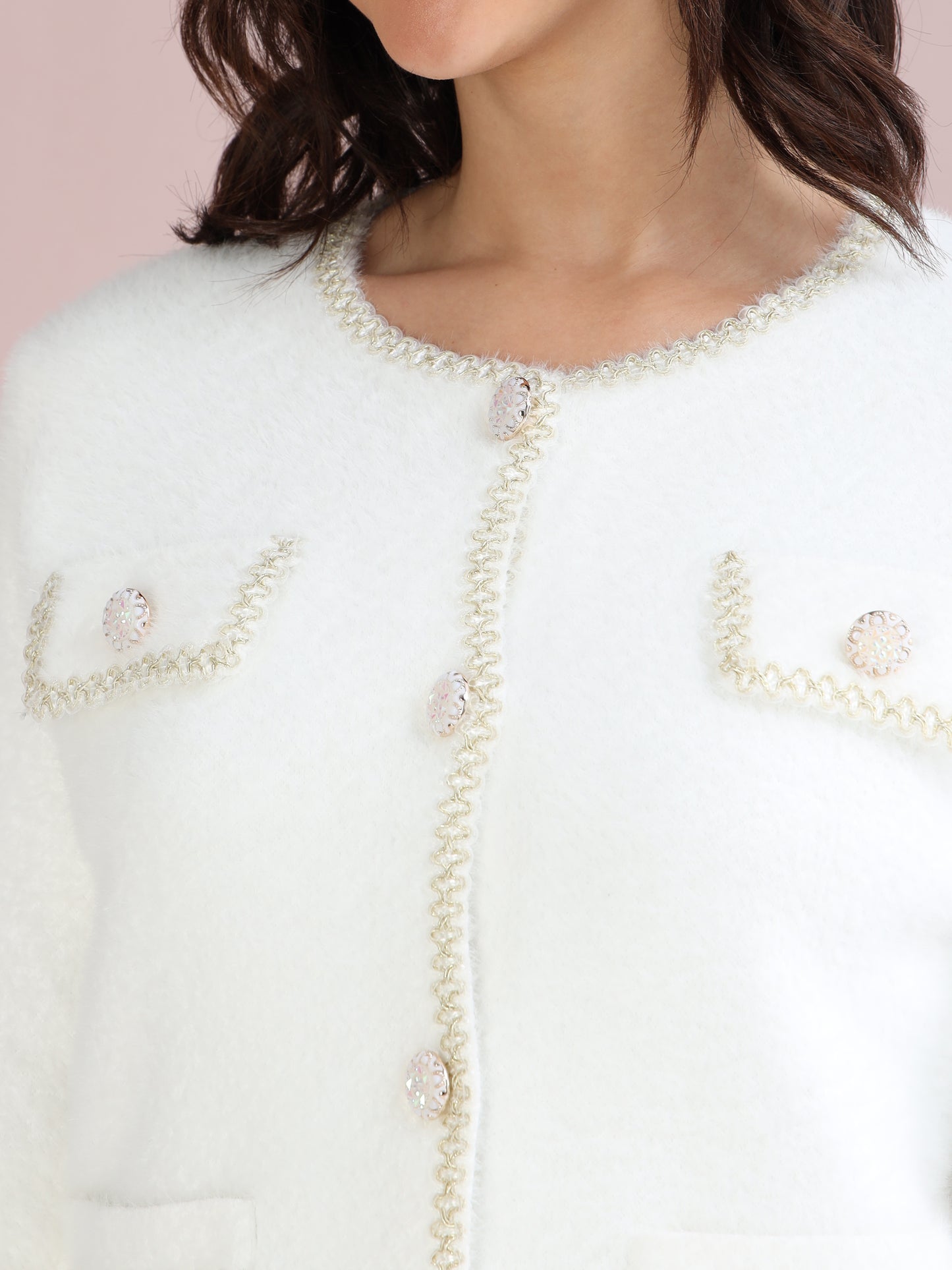Detailed close-up of pearl buttons and golden trim on a white women’s cardigan sweater.