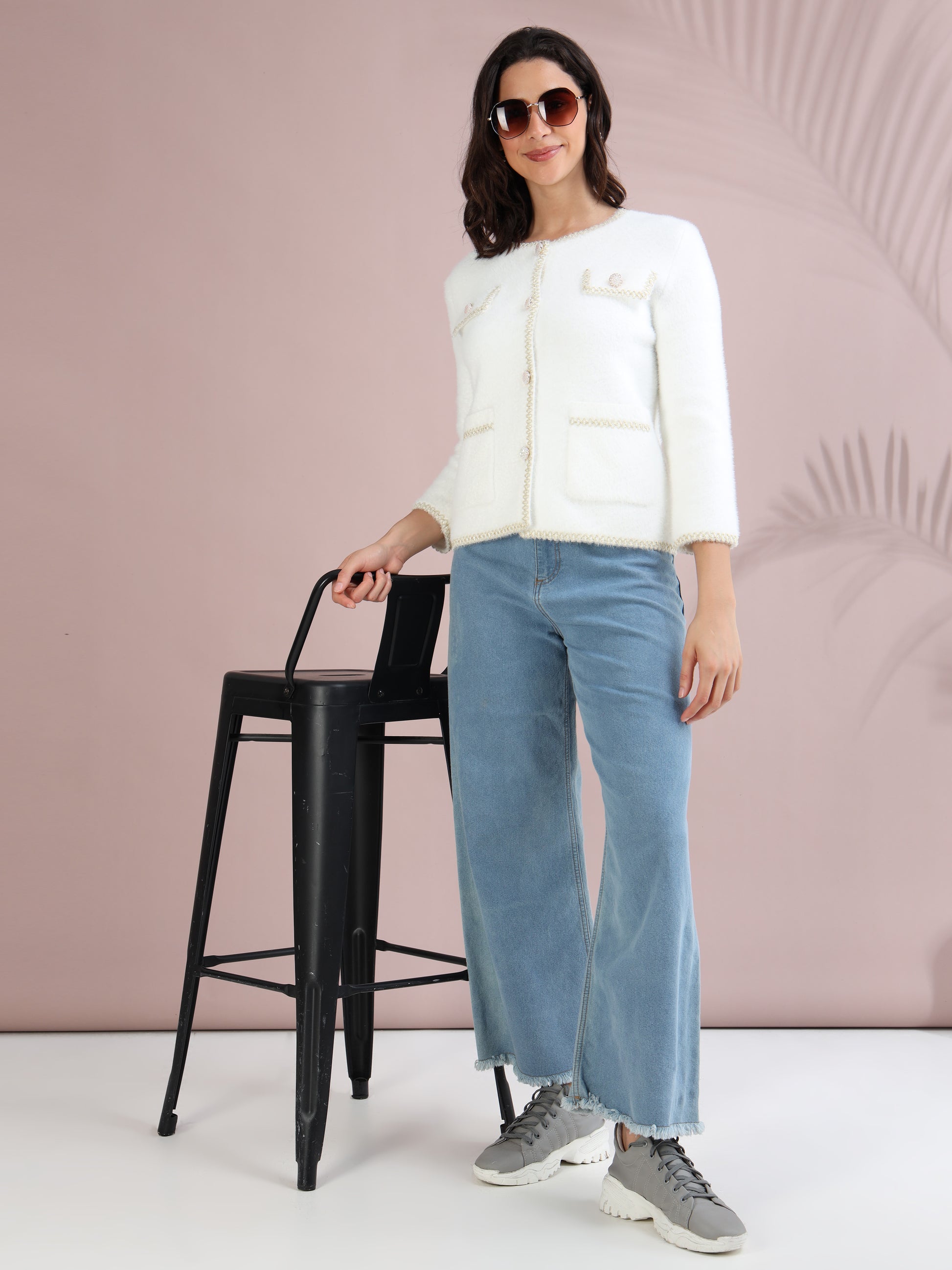 Woman styling a white cardigan sweater with wide-leg jeans, grey sneakers, and sunglasses for a chic winter outfit.