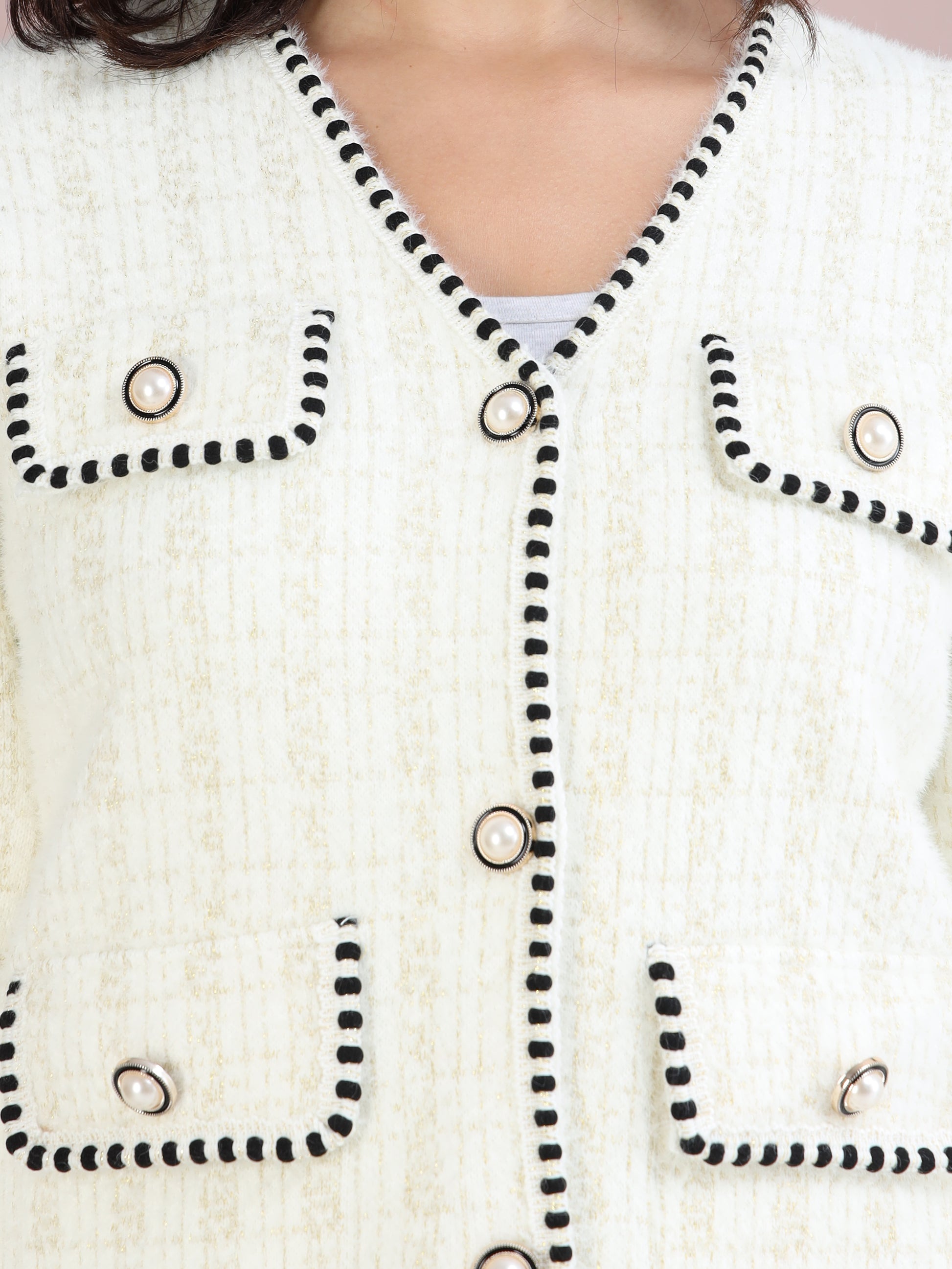 Detailed close-up of pearl button and black piping design on white tweed cardigan.