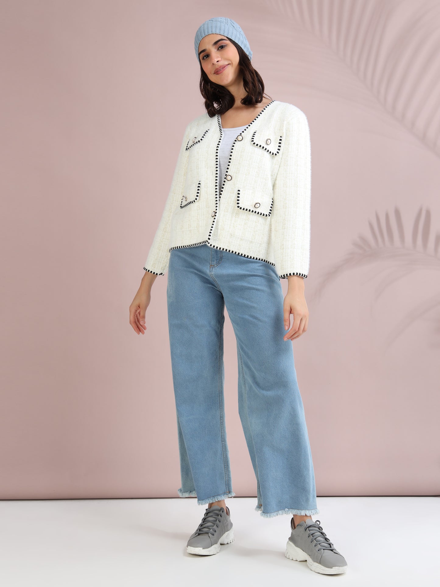 Woman styling a white tweed cardigan with blue wide-leg jeans, sneakers, and winter beanie hat.