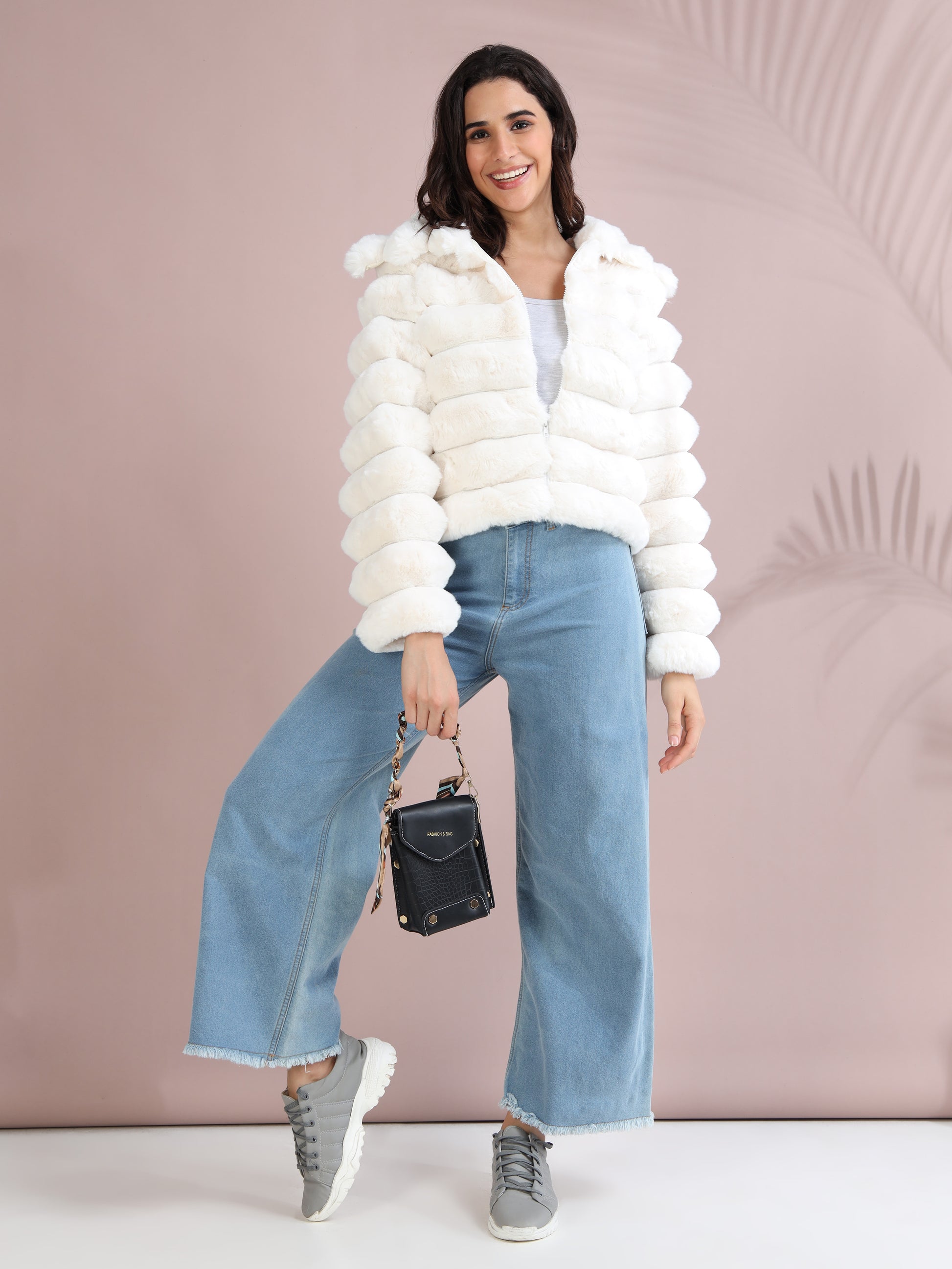 woman in white faux fur jacket, wide-leg jeans, grey sneakers, and black handbag.