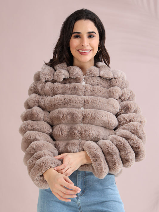 Woman wearing a beige faux fur winter jacket with horizontal padded design, paired with blue denim jeans.
