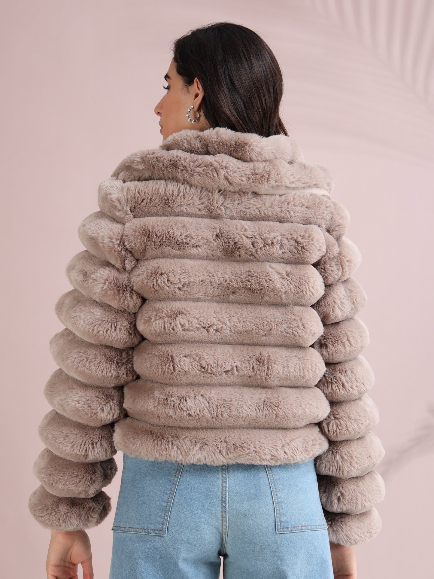 Back design of beige faux fur winter coat with ribbed padded layers, styled with blue jeans.