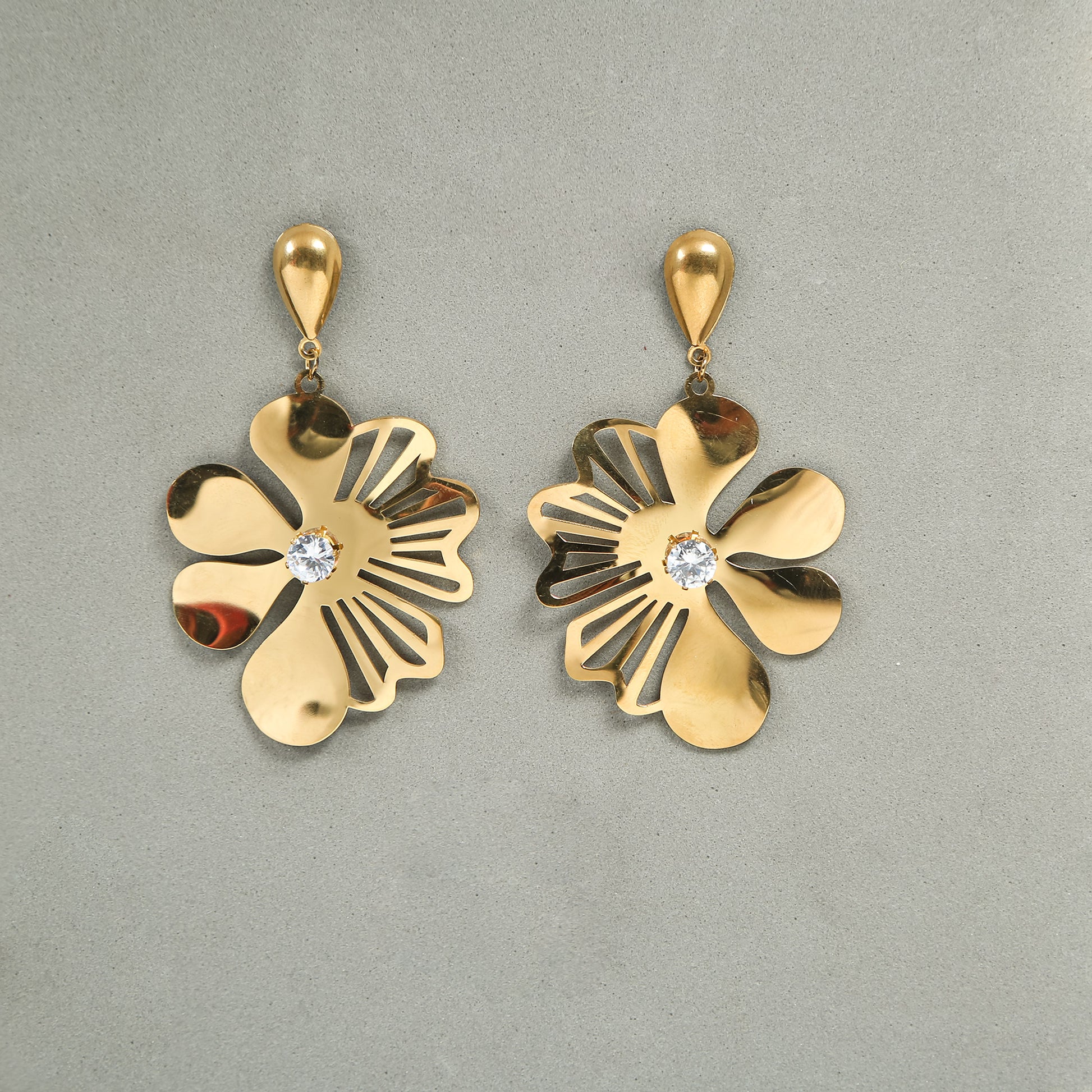 Gold floral drop earrings with cut-out petal design and crystal center displayed