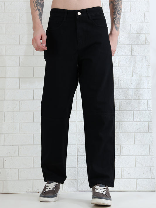 A person standing against a white brick wall wearing black denim pants and casual shoes.