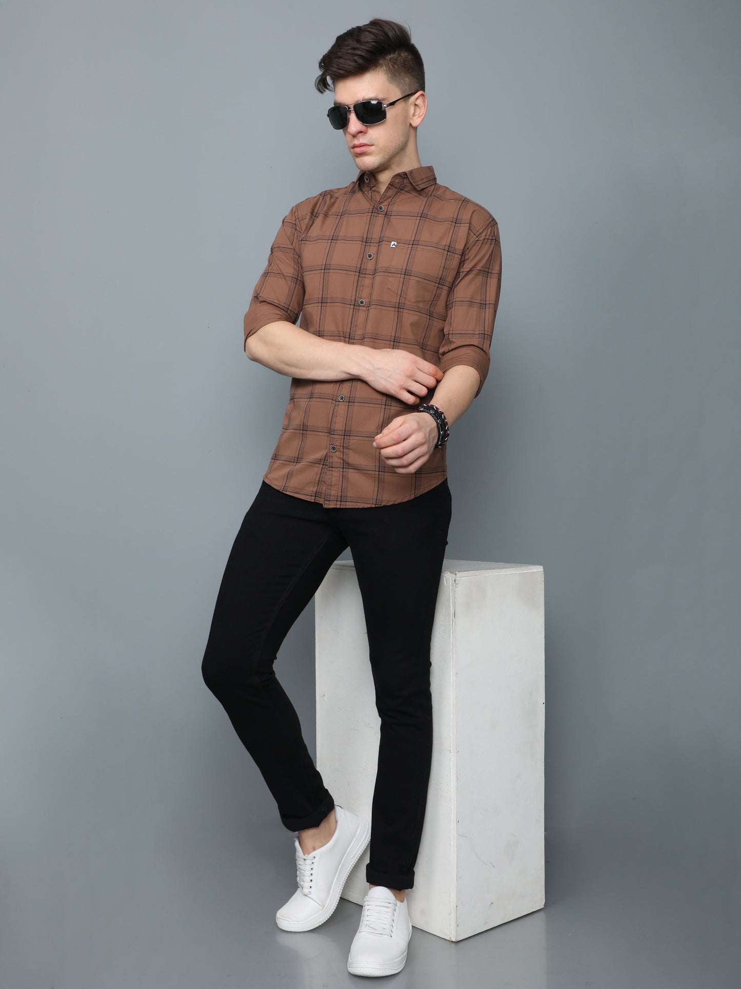 Men, brown checks shirt styled with black slim-fit jeans, white sneakers, and sunglasses.