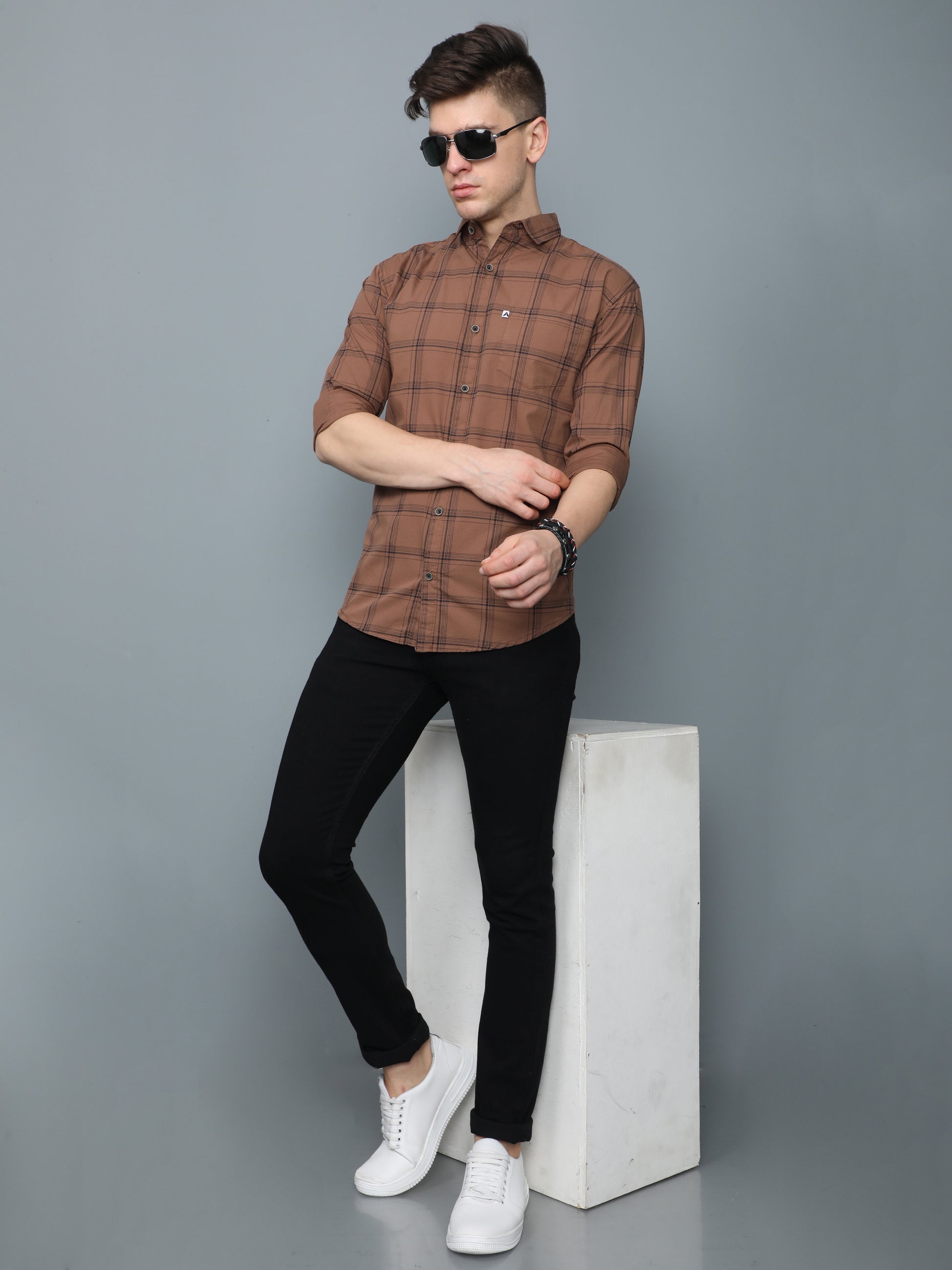 Men, brown checks shirt styled with black slim-fit jeans, white sneakers, and sunglasses.