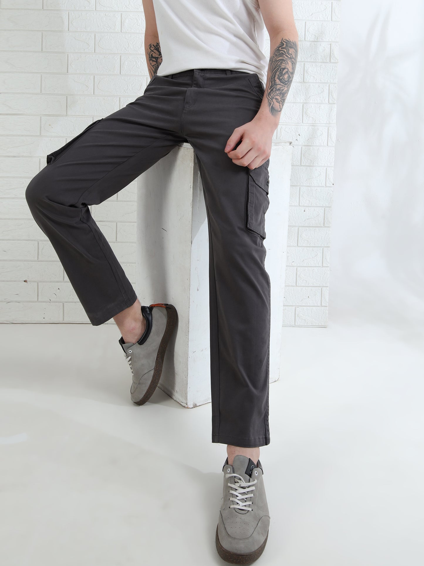 A person wearing dark grey cargo pants with six pockets, a white t-shirt, and gray shoes.