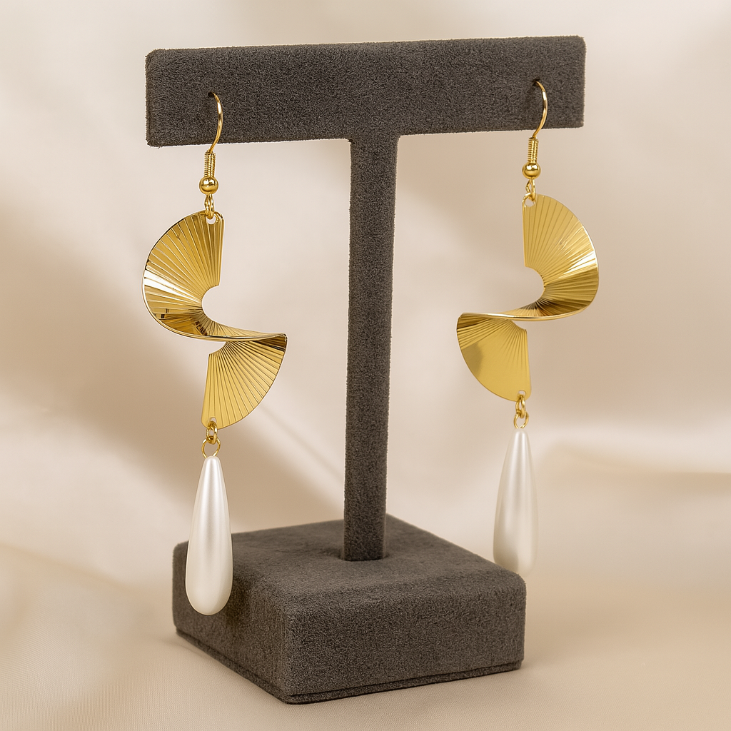 Gold earrings with white teardrop pendants on a gray stand against a beige background