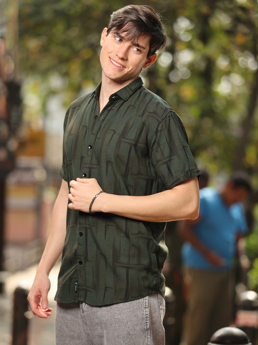A man wearing a green rayon cotton printed shirt with half sleeves.