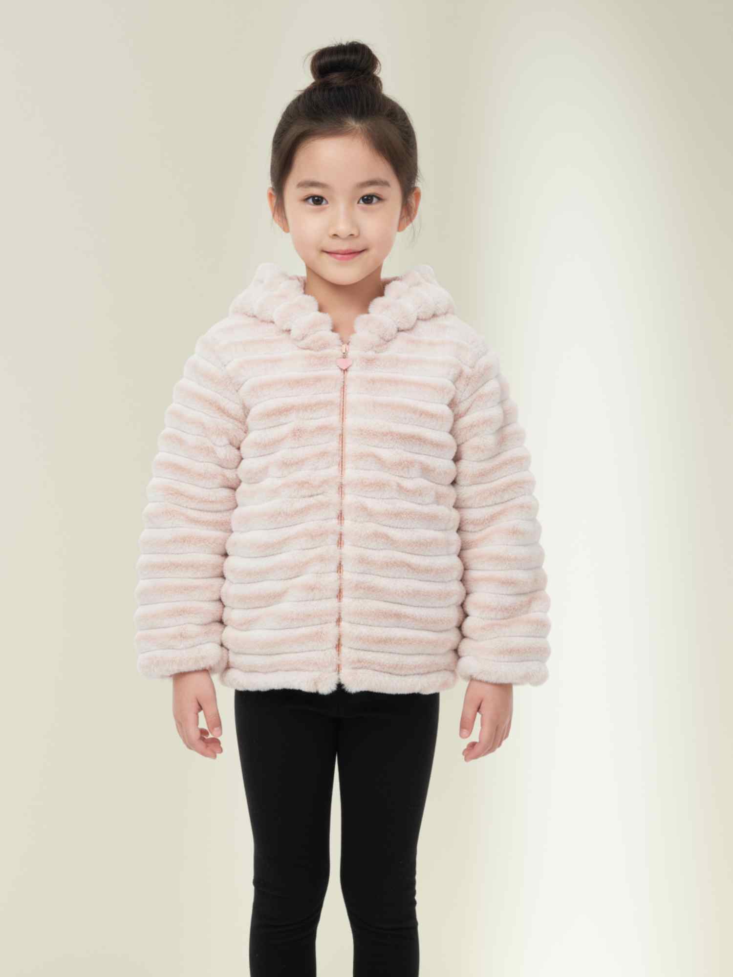 A young girl wearing a soft pink fur hooded winter jacket, unzipped with hands in pockets, paired with a white t-shirt and black leggings