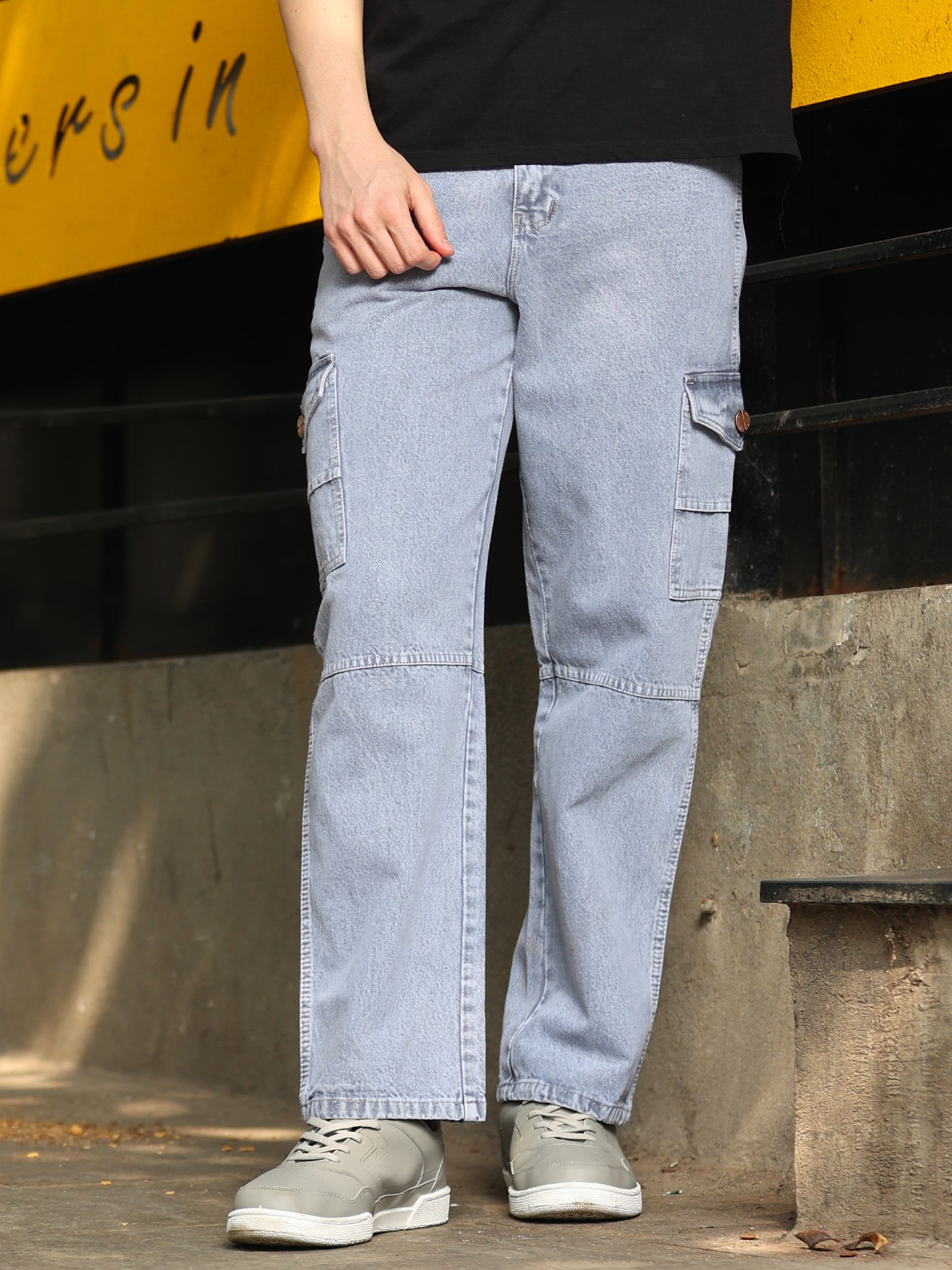 A person standing on the street wearing mid-grey relaxed fit jeans with a button closure and four pockets.
