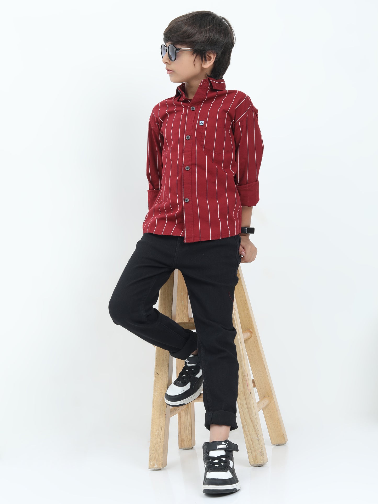 Person wearing a red striped shirt and black pants sitting on a wooden stool against a white background