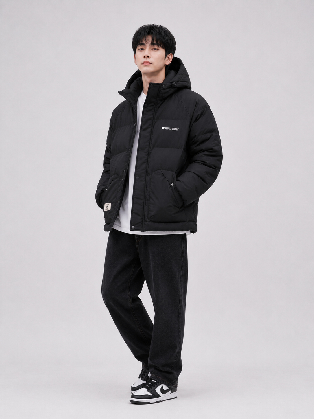 a black hooded puffer jacket with insulated padding, relaxed-fit dark denim jeans, and sneakers, styled for casual winter and streetwear fashion.