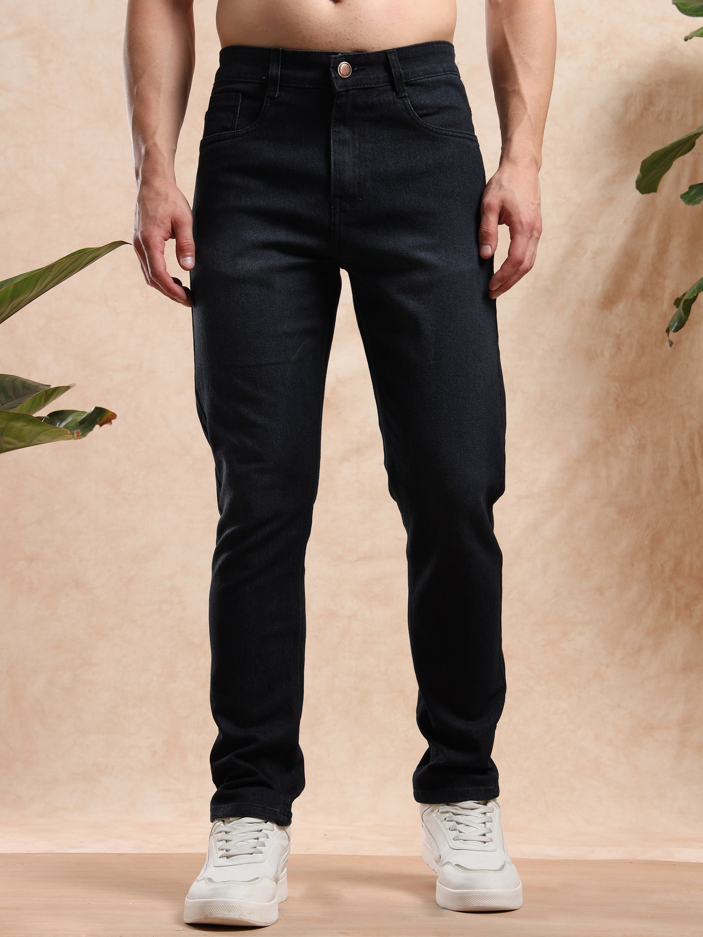 Person wearing black jeans and white sneakers against a beige background
