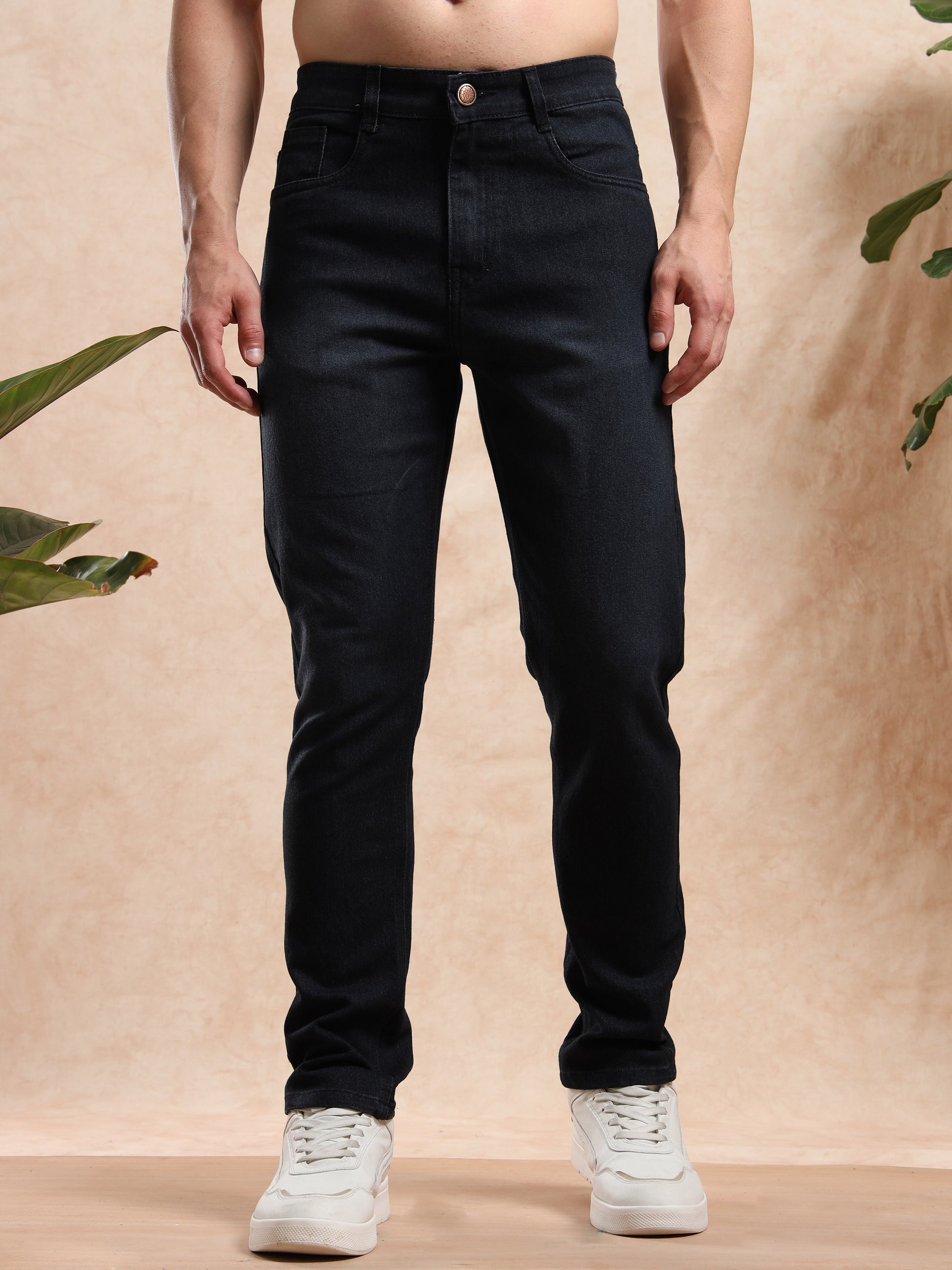 Person wearing black jeans and white sneakers against a beige background