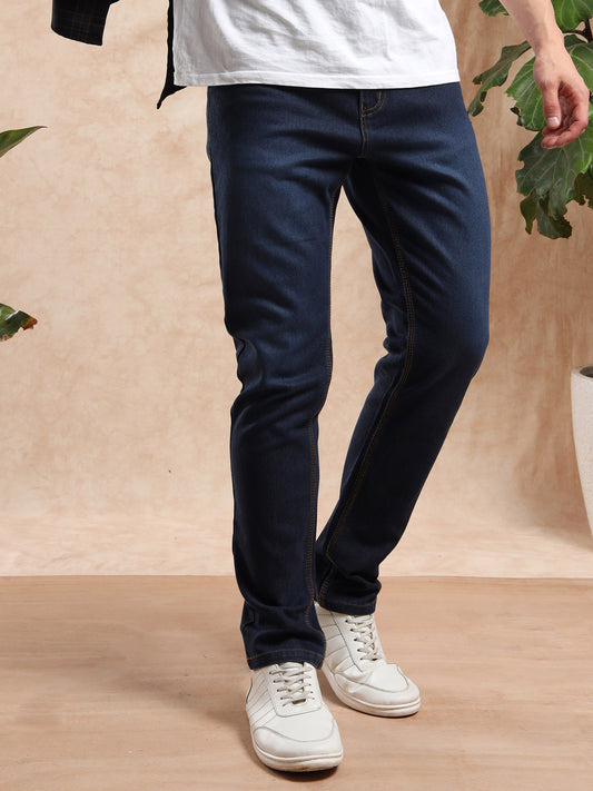 Person wearing navy blue pants and white sneakers on a wooden floor with a beige wall and green plants in the background.
