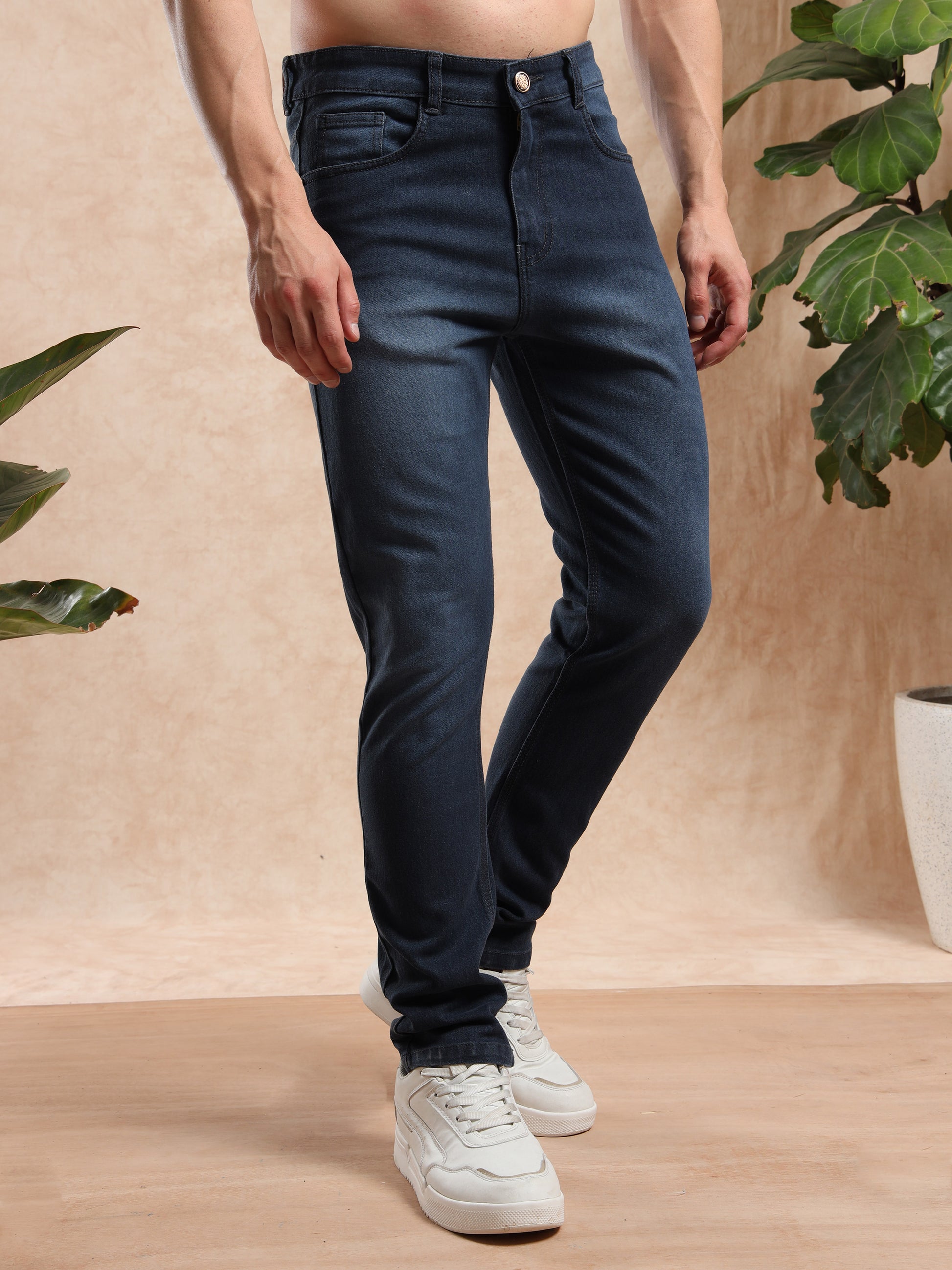 Trendy men, tapered dark blue jeans styled with casual shoes, angled front view.