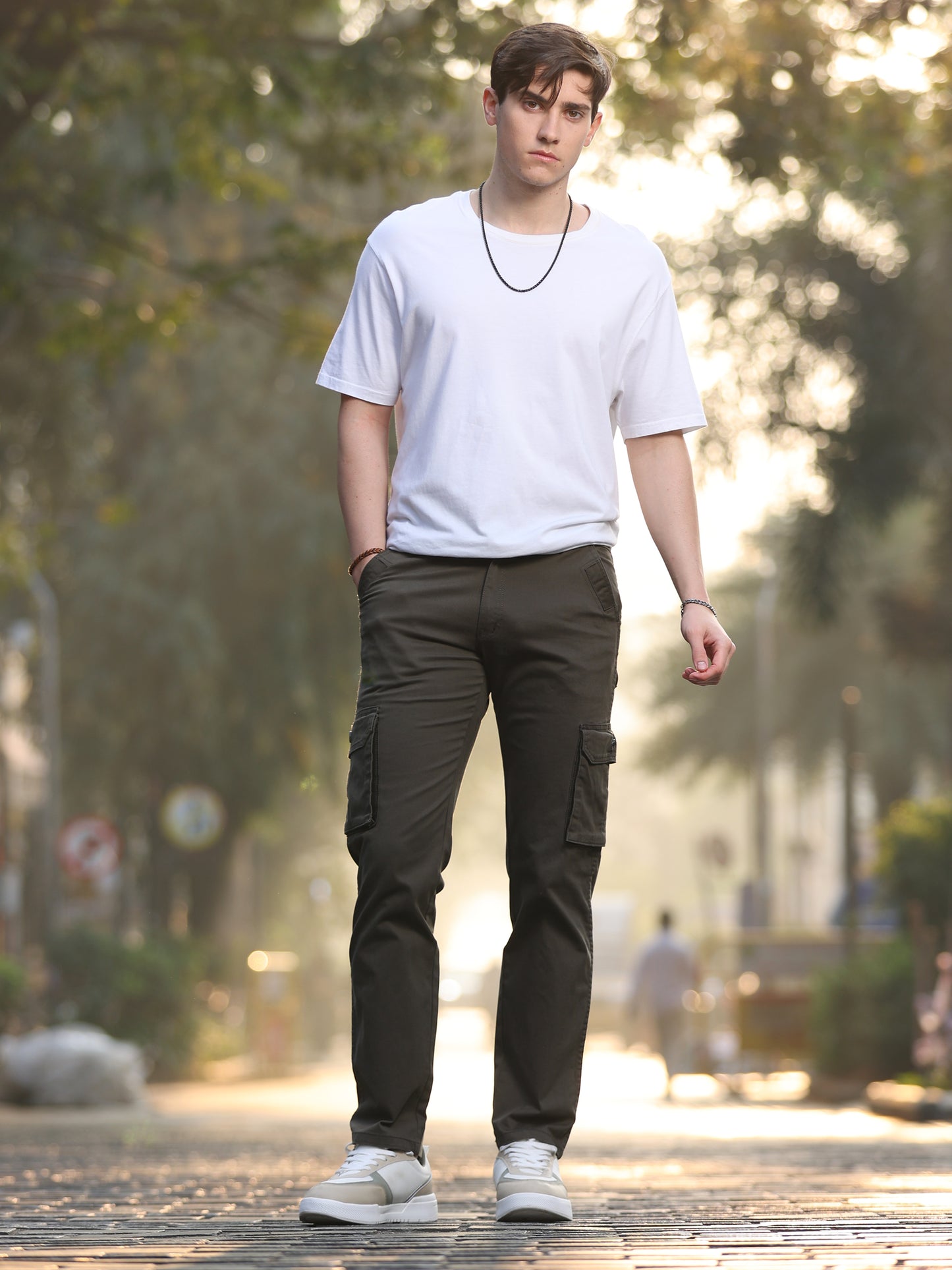 A person wearing a white t-shirt and olive cargo pants standing outdoors.