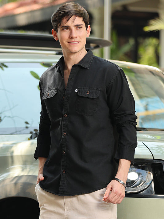 A man wearing a black long-sleeve denim shirt with a regular collar, featuring two chest pockets, buttoned cuffs, and a relaxed fit.