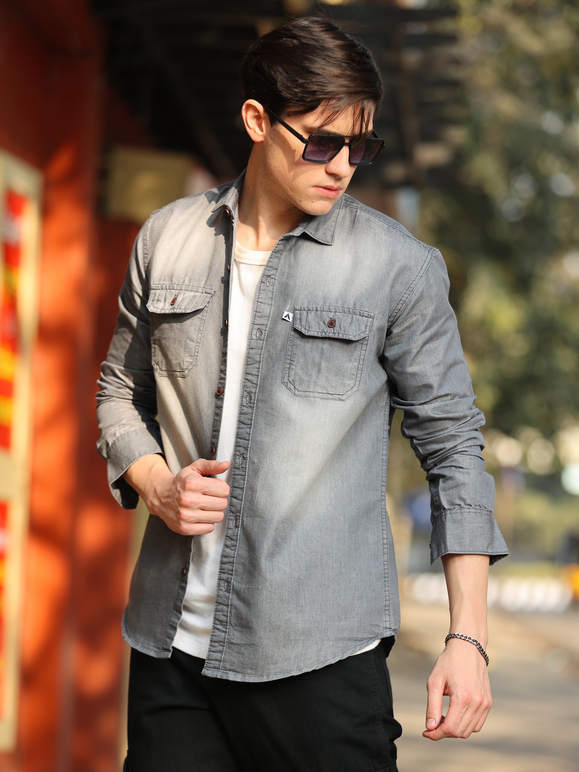 A man wearing a long-sleeved, collarless, blue denim shirt with two chest pockets, buttoned cuffs, and a relaxed fit.